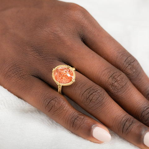Gold ring with a sunstone stone on a person's finger against a neutral background