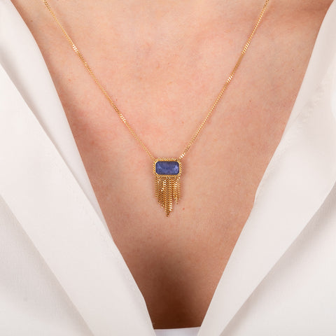 Gold necklace with a tanzanite gemstone on a person wearing a white top.