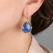 Gold earrings with blue tanzanite gemstones worn by a person