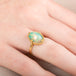 Gold ring with an Ethiopian opal gemstone on a person's finger
