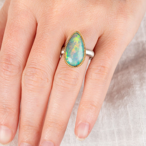 Hand wearing an Ethiopian opal teardrop ring with gold bezel and silver band