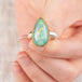 Close up of a hand holding an Ethiopian opal teardrop ring with gold bezel and silver band