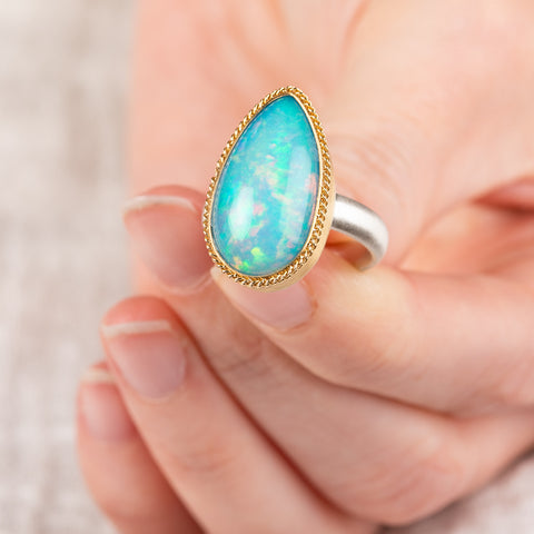 Hand holding an Ethiopian opal ring with 18k gold bezel and sterling silver band