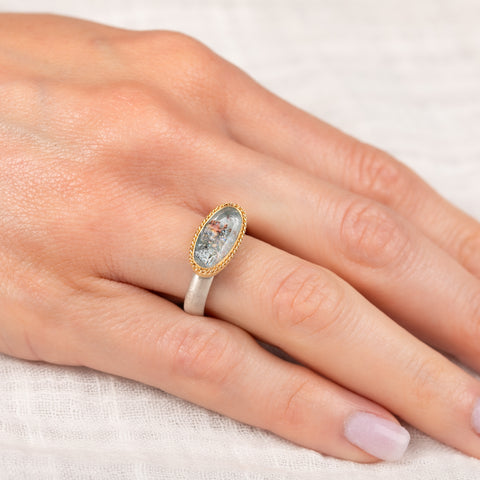 Gold and silver ring with a topaz gemstone on a hand against a white background