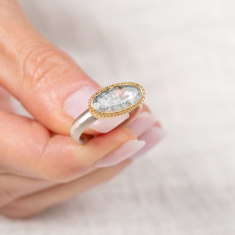 Gold and silver ring with a topaz gemstone held by a hand against a light background