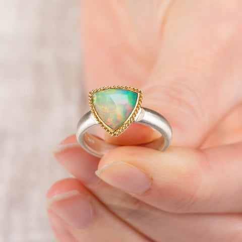 Close up of hand holding an Ethiopian opal ring with 18k gold bezel and sterling silver band