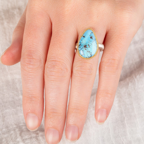 Hand wearing an turquosie teardrop ring with gold bezel and sterling silver ring