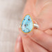 Close up of hand holding a turquosie teardrop ring with gold bezel and sterling silver ring