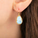 A close-up of a gold dangle earring with a light blue turquoise stone, worn on a person's ear.