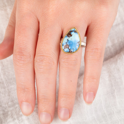 Hand wearing a turquoise teardrop ring with gold bezel and sterling silver band