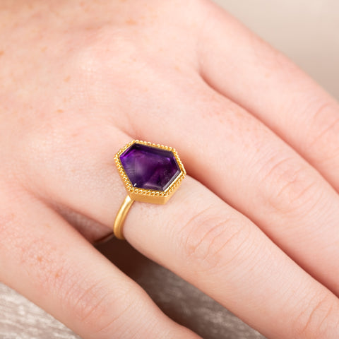 Gold ring with an amethyst gemstone on a person's finger