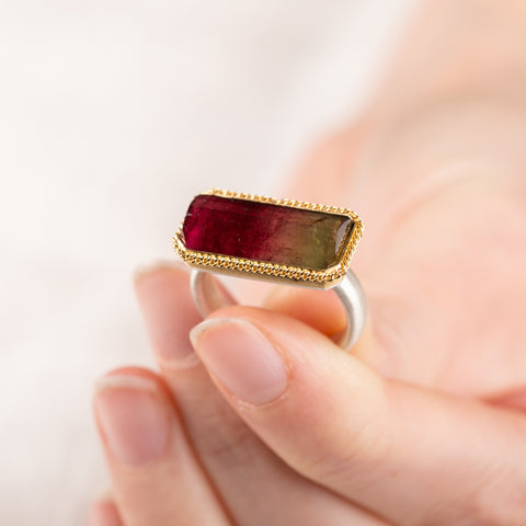 Close up of hand holding a watermelon tourmaline ring with gold bezel and silver band