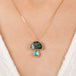 Gold necklace with a mushroom pendant featuring boulder opal and aquamarine stones on a person