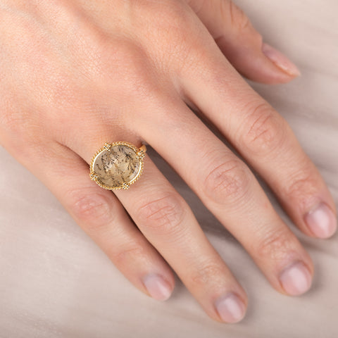 Gold ring with a dendritic quartz stone and intricate design on a hand