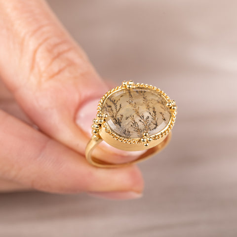 Gold ring with a dendritic quartz stone and intricate design held in hand