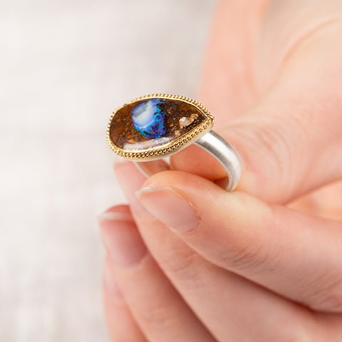 A hand holding a Yowah nut opal ring with an 18k gold bezel and sterling silver band
