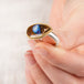 A hand holding a Yowah nut opal ring with an 18k gold bezel and sterling silver band