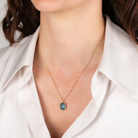 Gold necklace with an oval aquamarine pendant worn by a person in a white shirt