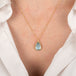 Gold necklace with a teardrop-shaped aquamarine pendant on a person wearing a white blouse