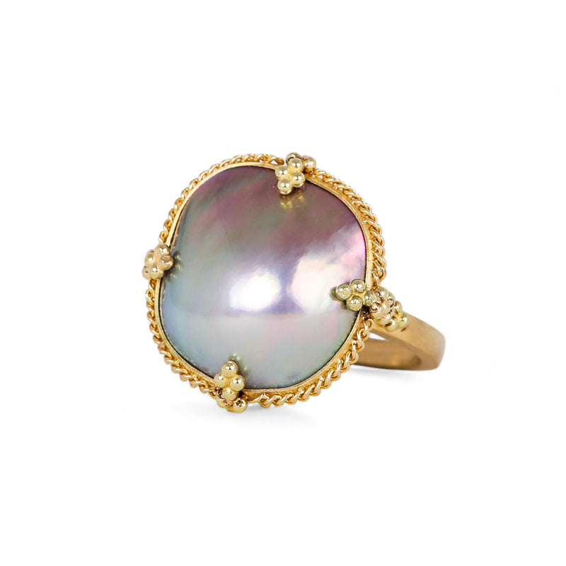 A one-of-a-kind iridescent pearl ring with blue, grey and purple hues is set in a chain wrapped 18k yellow gold bezel with four beaded prongs on a thin gold band.