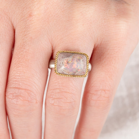 A person wears a handcrafed ring featuring a mexican opal gemstone in an 18k gold setting with a sterling silver band