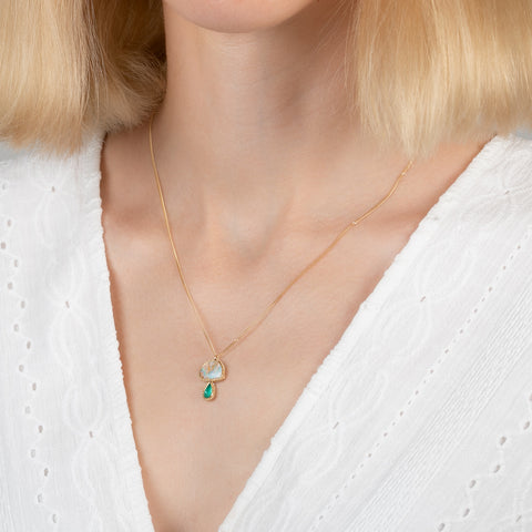 Gold necklace with a mushroom pendant featuring opal and emerald stones on a person