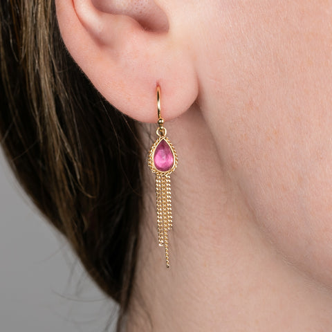 A person wears handmade pink tourmaline and 18k gold earrings with gold tassels