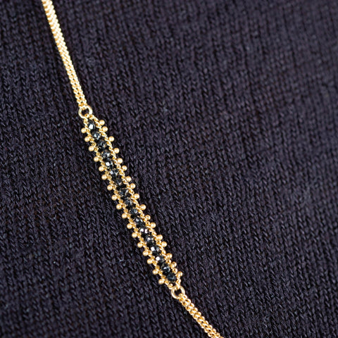 A close-up of a long 18k yellow gold necklace that features an off-center row of black diamond beads.