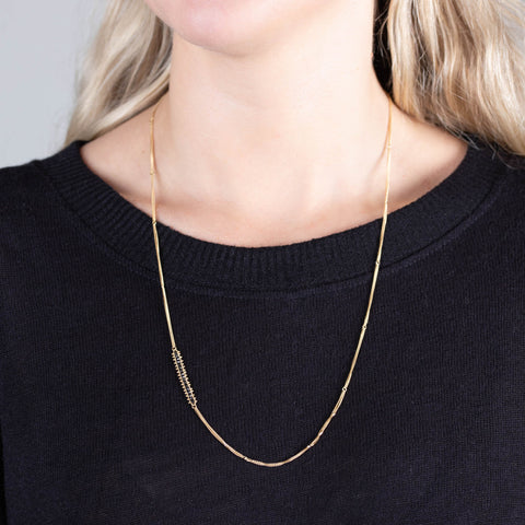 A model wears a long 18k yellow gold chain necklace that features an off-center row of woven black diamond beads.