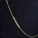 A close-up of a long 18k yellow gold necklace that features an off-center row of silver diamond beads.