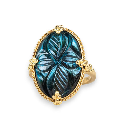 Labradorite ring in 18K yellow gold, featuring intricate floral carvings. Dark blue ink shifts to cerulean flashes upon the hand-carved gemstone's surface. Encased in a handmade gold bezel.