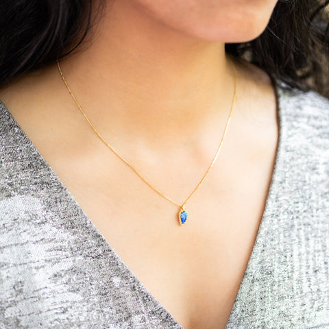 A model wears a hand-carved leaf pendant from a glowing blue Moonstone, encased in a unique handmade gold bezel with braided detail. Suspended on an 18k yellow gold chain, offering meticulous craftsmanship and elegance. Handmade in New York.