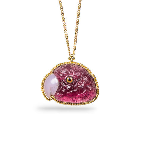 Tourmaline parrot pendant in 18K yellow gold, hand-carved from magenta pink stone. Detailed feathers, eyes, and Pink Opal beak. Set in a handmade gold bezel with braided detail, suspended from an 18K yellow gold chain.