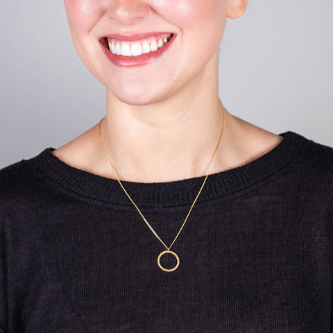 A model wears a delicate 18k yellow gold chain necklace with a small circle pendant crafted in chain to create a stardust-like effect 