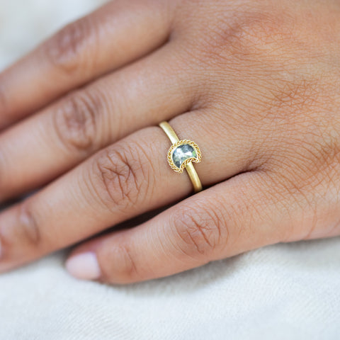 A model wears a diamond crescent moon ring in 18K yellow gold. Symbolizing hope and new beginnings, set in a handmade crescent-shaped gold bezel with braided detail. Handmade in New York.