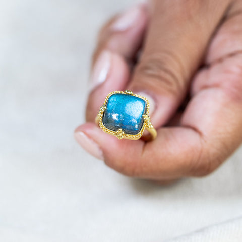 A model holds a Labradorite ring in 18K yellow gold with luminescence, reminiscent of moonbeams. Handmade bezel encases the gem in 18k yellow gold with a braided detail and granulated prongs.
