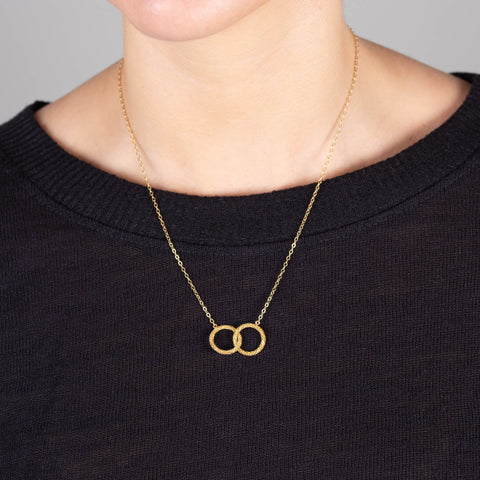 A model wears a short pendant with two interlocking 18k yellow gold circles that is set in a delicate chain.