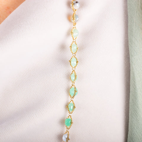 A close up of a mixed opal bead necklace featuring teal stones that are woven with 18k yellow gold chain. 