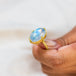 Moonstone ring in 18K yellow gold, showcasing swirling blue iridescence. Hand-crafted gold setting displays intricate braided detail and granulated prongs. Handmade in New York.