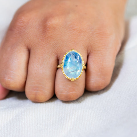 A model wears a Moonstone ring in 18K yellow gold, revealing a captivating blue iridescence. Hand-crafted gold setting with braided detail and granulated prongs. Handmade in New York.