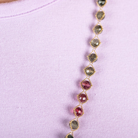A close-up of a  green and pink tourmaline bead necklace woven with 18k yellow gold chain