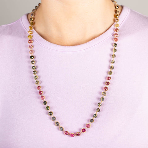 A model wears a long woven 18k yellow gold necklace that features green and pink tourmaline gemstone beads throughout