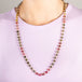 A model wears a long woven 18k yellow gold necklace that features green and pink tourmaline gemstone beads throughout