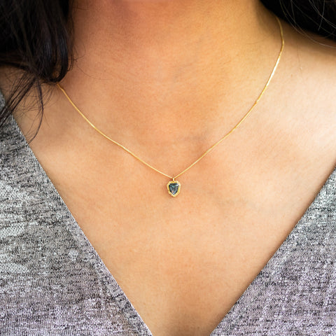 A model wears a black diamond pendant in 18k yellow gold bezel, suspended from an 18K yellow gold chain and is set in a unique design with handmade gold bezel and braided detail. Handmade in New York.