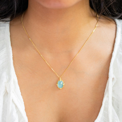 A model wears an oval Aquamarine pendant in 18k yellow gold bezel, adorned with braided gold accents and granulated prongs. Handmade in New York