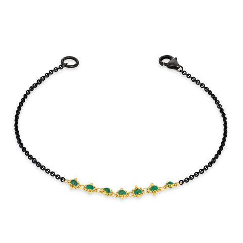 This oxidized sterling silver bracelet features a row of green emeralds suspended in 18k yellow gold chain in the center.