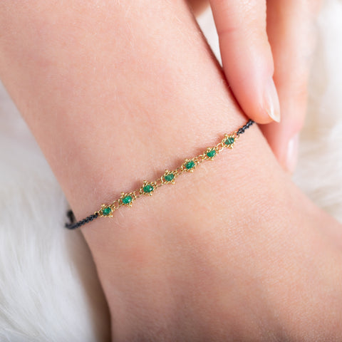 A close-up of an oxidized sterling silver bracelet that features a row of green emeralds suspended in 18k yellow gold chain in the center.