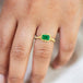 A model wears this Emerald ring in 18K yellow gold, capturing the play of light akin to morning dewdrops on green grass. Intricate frame of shimmering golden chain and delicate beaded prongs. Handmade in New York. 