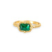 Emerald ring in 18K yellow gold, showcasing tiny facets reflecting light like morning dewdrops on green grass. Encased in an intricate frame of shimmering golden chain and delicate beaded prongs.