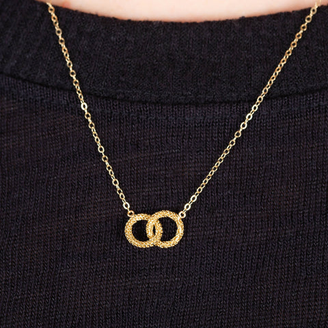 A close up of a petite 18k yellow gold interlocking circle necklace made with a diamond cut chain.
